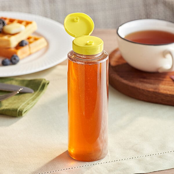 A 11 oz. clear PET sauce bottle with a yellow cap next to a plate of waffles and a cup of tea.