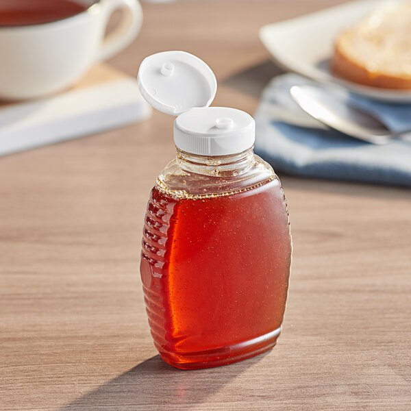 A Classic Queenline PET bottle of honey with a white cap on a table.