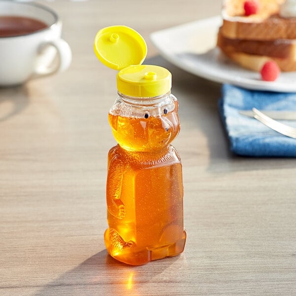 A honey bear bottle with a yellow cap on a table next to a plate of toast.
