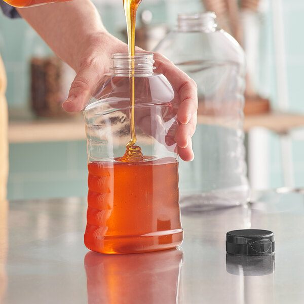 A person pouring honey into a ribbed hourglass PET honey bottle.