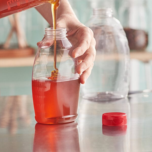 A person pouring honey into a Classic Queenline PET honey bottle with a red cap.
