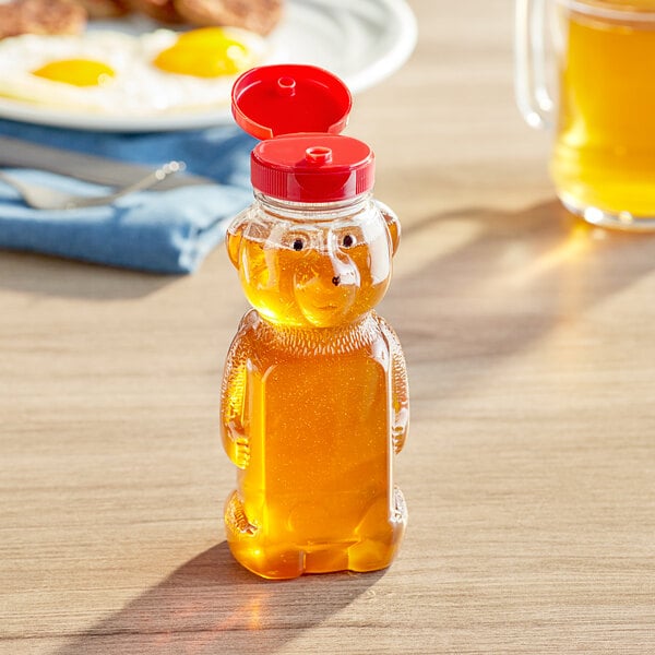 A plastic bear shaped honey bottle with a red lid on a table.