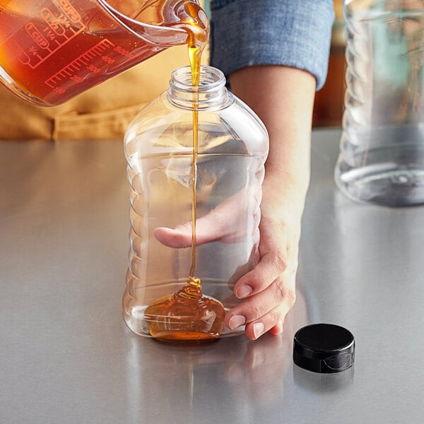 A person pouring honey into a Ribbed Hourglass PET honey bottle.