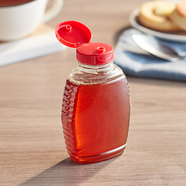 A Classic Queenline PET honey bottle with a red cap sitting on a table.