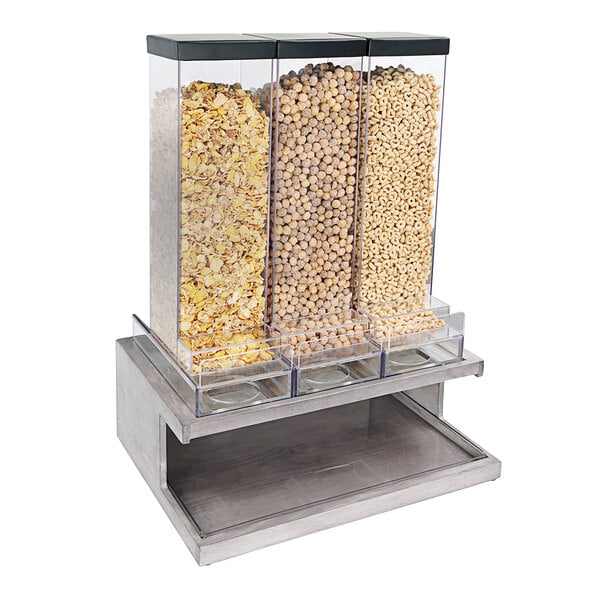 A Cal-Mil gray metal triple canister cereal dispenser on a counter filled with different types of cereals.