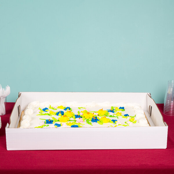 The bottom of a white Baker's Mark full sheet bakery box containing a cake with frosting flowers.
