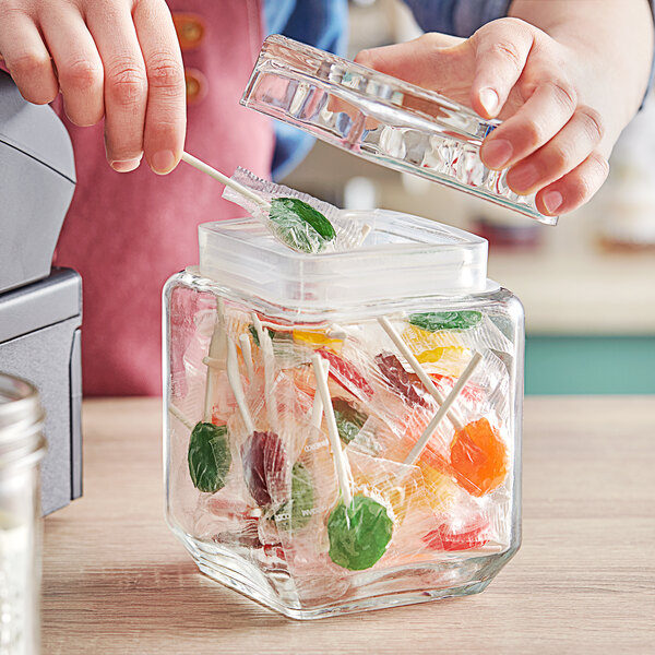 A person putting a lollipop into a clear glass jar.