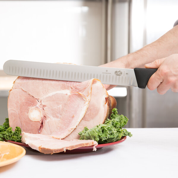 A person cutting a ham with a Victorinox Granton Edge Slicing Knife.