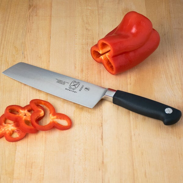 A Mercer Culinary Genesis Forged Nakiri Knife next to sliced bell peppers on a cutting board.