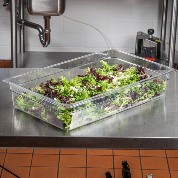 A clear plastic Cambro food pan with green and red lettuce in it on a counter.