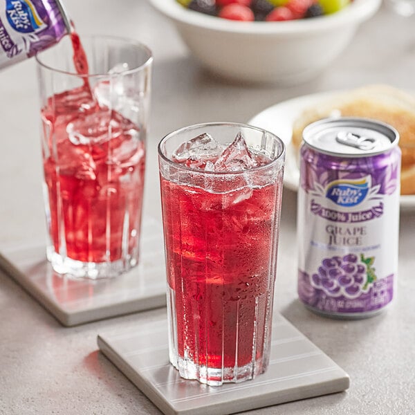 A can of Ruby Kist grape juice being poured into a glass of red liquid with ice.