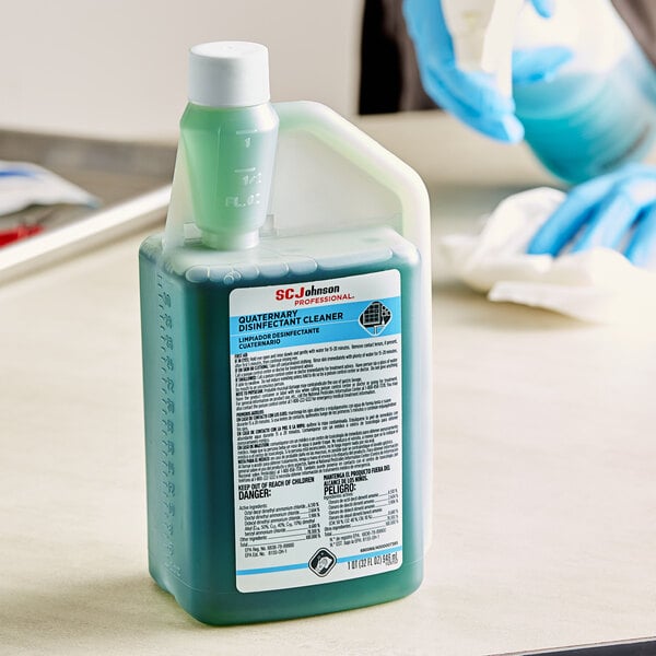A blue and white bottle of SC Johnson Professional Quaternary Disinfectant Cleaner with a green lid sitting on a counter.