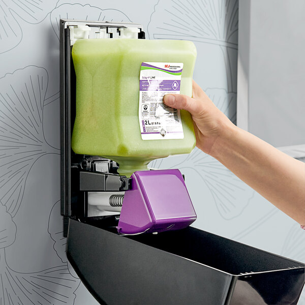 A person using a green SC Johnson Professional Solopol Lime Hand Soap refill to fill a purple dispenser.
