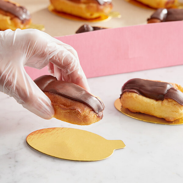 A hand placing a chocolate covered pastry on a gold oval dessert board with a tab.