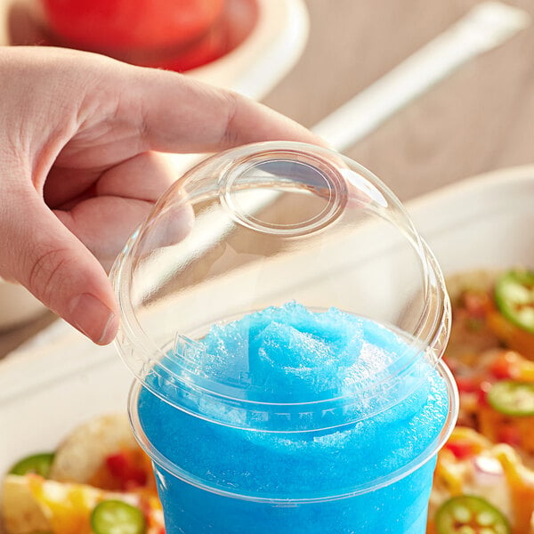 A hand placing a World Centric compostable dome lid on a plastic cup with blue liquid inside.