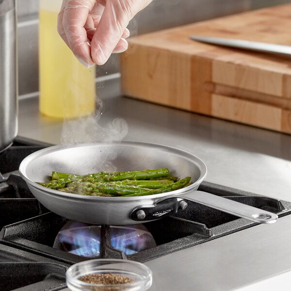 A person cooking green asparagus in a Vollrath Wear-Ever aluminum fry pan on a stove.