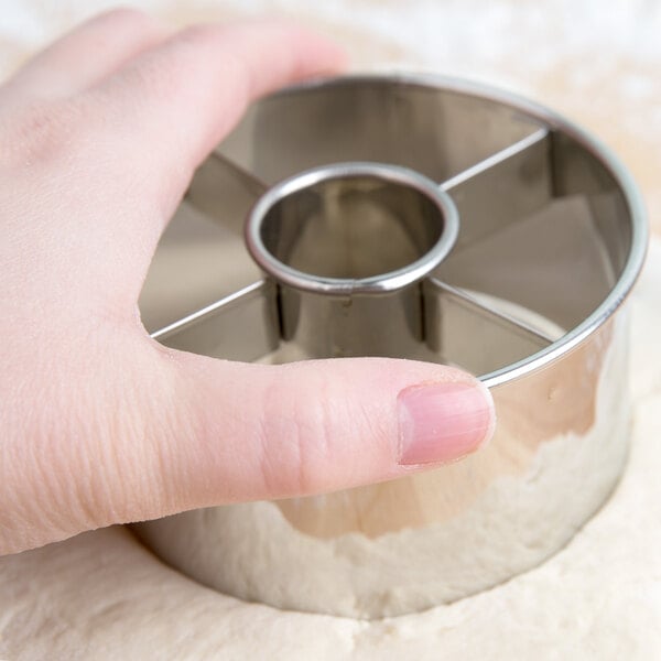 A hand holding a silver stainless steel Ateco doughnut cutter.