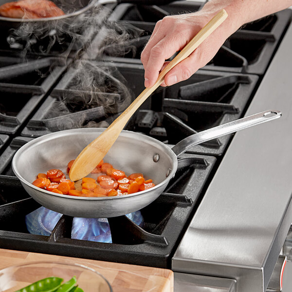 A person stirring food in a Vollrath aluminum fry pan on a stove.
