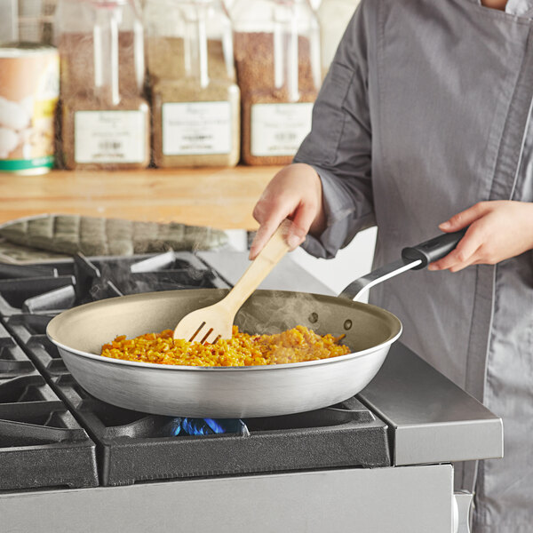 A woman using a Vollrath Wear-Ever aluminum non-stick fry pan to cook food on a stove.