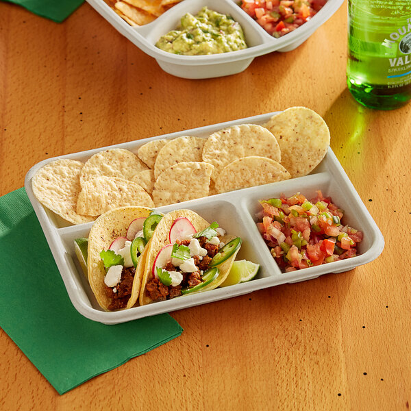 A World Centric compostable fiber tray holding tacos, chips, and salsa on a table.