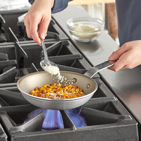 A person cooking corn in a Vollrath Wear-Ever non-stick fry pan on a stove.