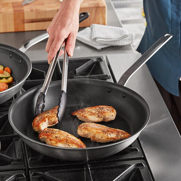 A person cooking food in a Vollrath Tribute non-stick fry pan.
