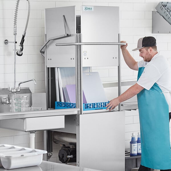 A man in a blue apron loading a Noble Warewashing tall dish washer.