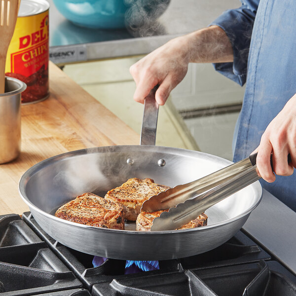 A person cooking meat in a Vollrath aluminum fry pan.