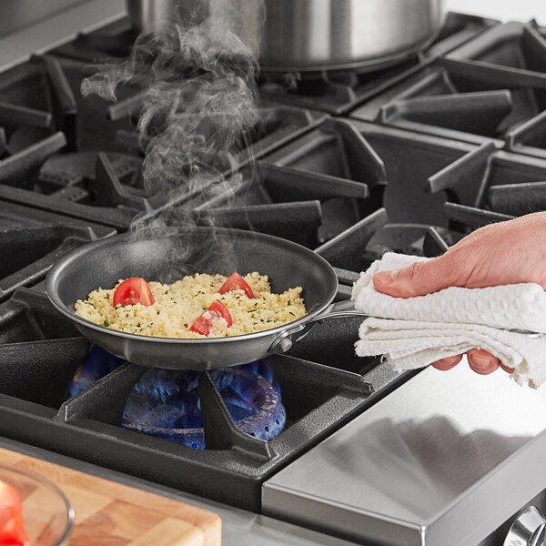 A person using a Vollrath Tribute stainless steel non-stick fry pan to cook food on a stove.