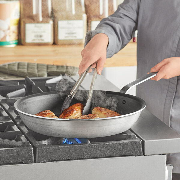 A person cooking food in a Vollrath aluminum non-stick fry pan with a plated handle.
