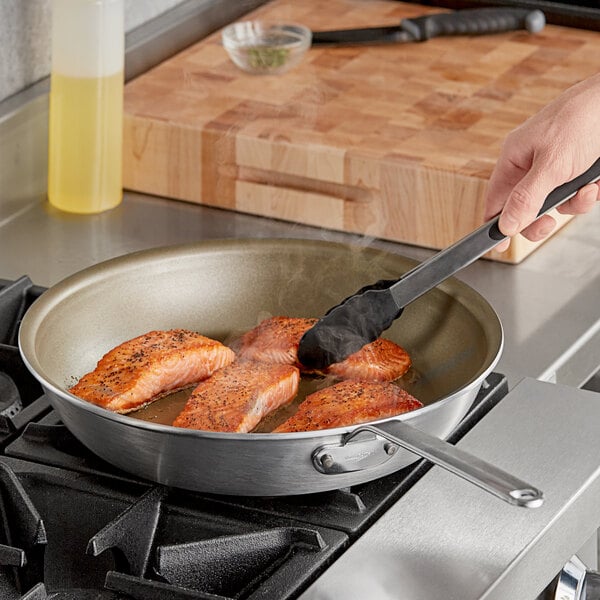 A person cooking salmon in a Vollrath Wear-Ever non-stick fry pan.