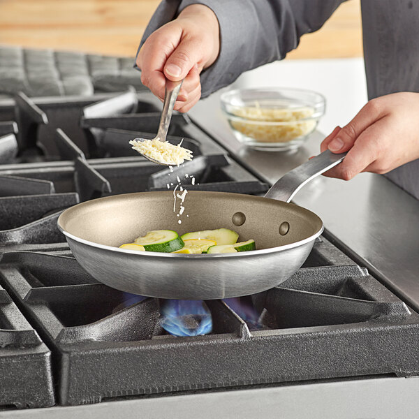 A person stirring cheese into zucchini in a Vollrath non-stick fry pan.