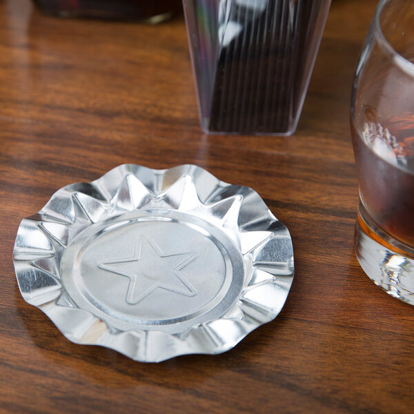 A Royal Paper aluminum foil ash tray with a silver star design on a counter next to a glass of liquid.