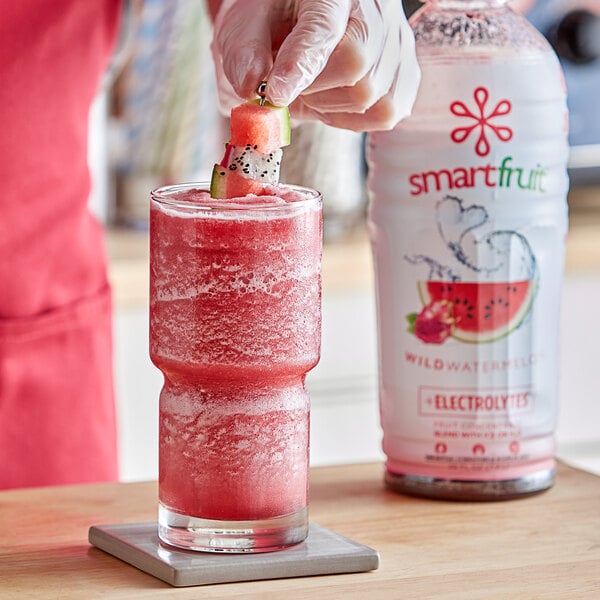 A person preparing a pink Smartfruit Wild Watermelon drink in a glass with a straw.