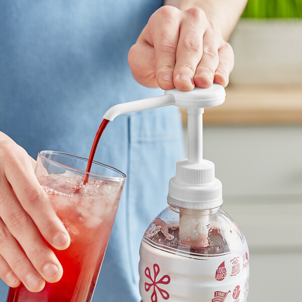 A hand using a Smartfruit Puree Pump to pour red liquid into a glass.