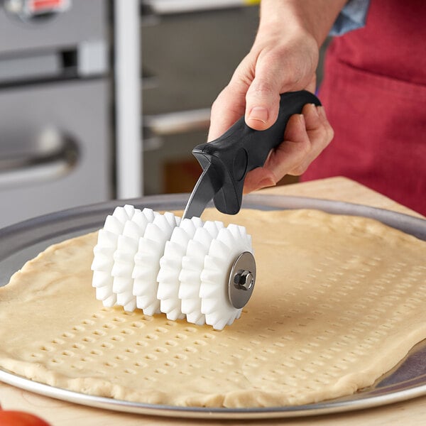 A person using a Choice dough docker with pointed wheels to cut dough.
