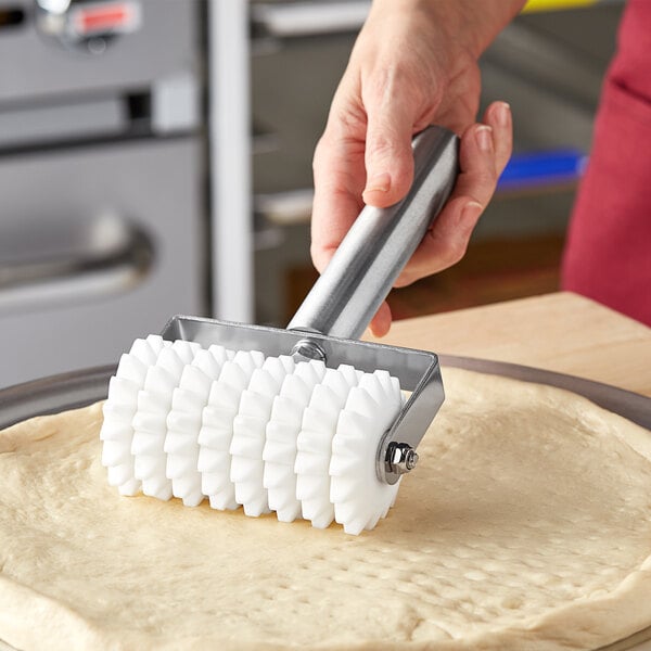 A person using a Choice stainless steel dough docker to dock pizza dough.