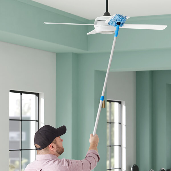 A man using a Lavex telescopic fan duster to clean a ceiling fan.