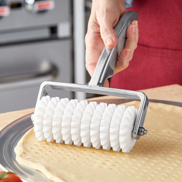 A person using a Choice dough docker with pointed wheels to roll out pizza dough.