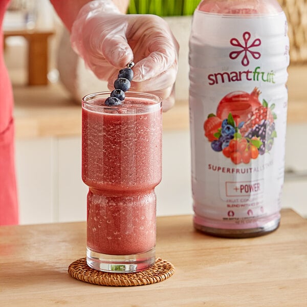 A person using a spoon to add Smartfruit Superfruit All-Stars puree to a smoothie.