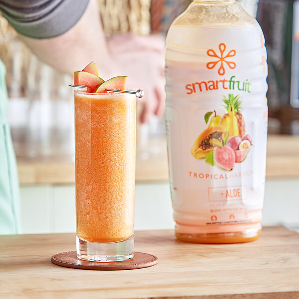 A plastic bottle of Smartfruit Tropical Harmony Puree next to a glass of fruity drink.
