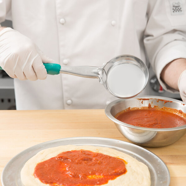 A person using a Vollrath teal spoodle to serve red sauce on a pizza.