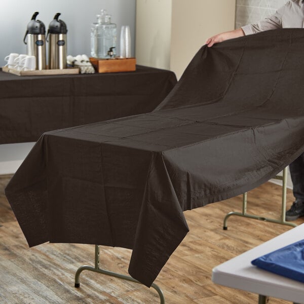 A person holding a brown Hoffmaster table cover over a table.