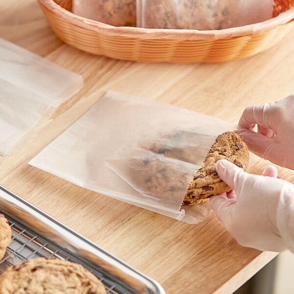 A person in gloves holding a cookie in a white wet waxed Choice sandwich bag.