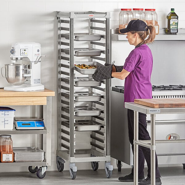 A woman in a professional kitchen assembling a Cambro Camshelving trolley rack.
