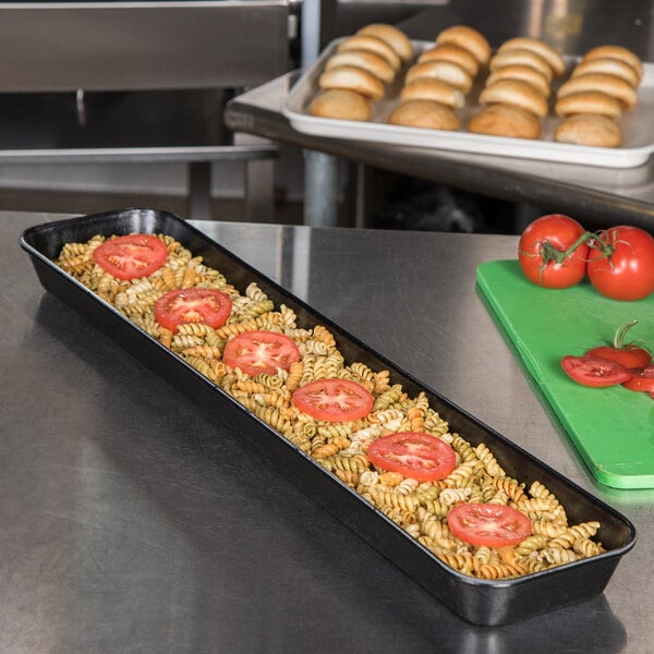 A Carlisle black fiberglass market tray with pasta and tomatoes on a counter.