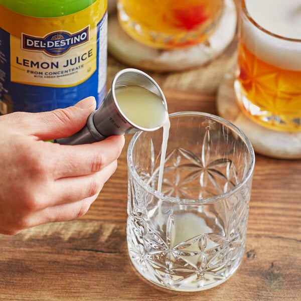 A hand pouring Del Destino Lemon Juice into a glass.