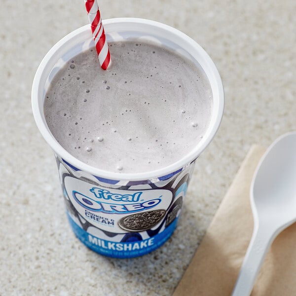 A cup of f'real Oreo Cookies and Cream milkshake with a straw and a spoon.