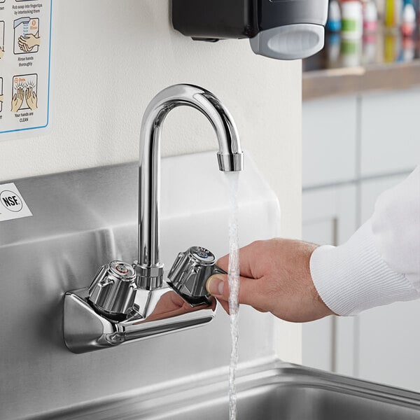 A person's hand pressing a Regency gooseneck faucet with water running over a white surface.