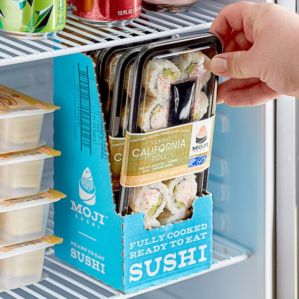 A hand holding a plastic container of Moji Classic California Roll sushi.